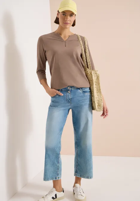 3/4-Arm Shirt mit Split Neck und Elastiksaum cocoa taupe Frau in hellbraunem 3/4-Arm-Shirt, hellblauen Culotte-Jeans, weißen Sneakers und Strohtasche vor neutraler Wand.