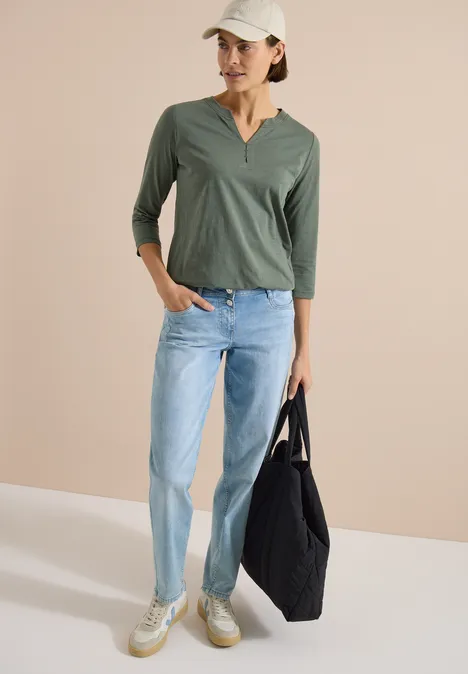 3/4-Arm Shirt mit Split Neck und Elastiksaum dried olive green Frau trägt einen olivgrünen 3/4-Ärmel-Pullover, helle Jeans, Sneakers und hält eine schwarze Tasche.