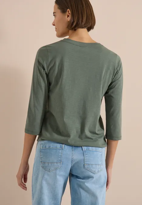 3/4-Arm Shirt mit Split Neck und Elastiksaum dried olive green Rückansicht einer Person mit grünem 3/4-Arm-Shirt und blauen Jeans vor beigem Hintergrund