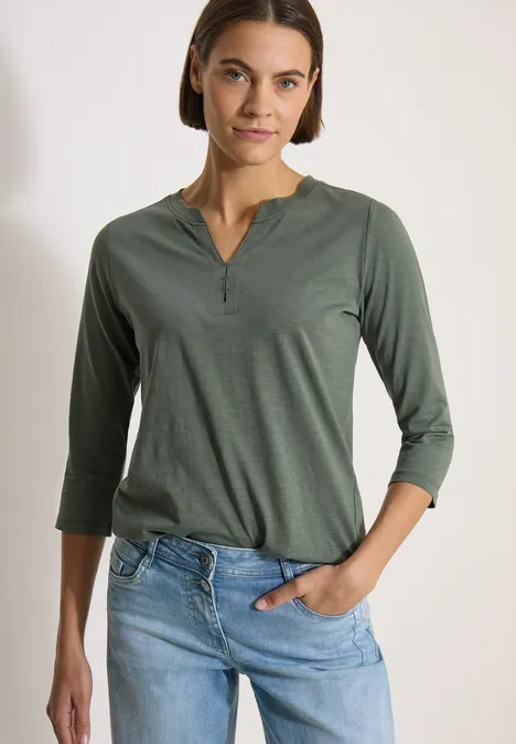 3/4-Arm Shirt mit Split Neck und Elastiksaum dried olive green Frau trägt grünes Shirt mit 3/4-Ärmeln und V-Ausschnitt, halb in helle Jeans gesteckt.