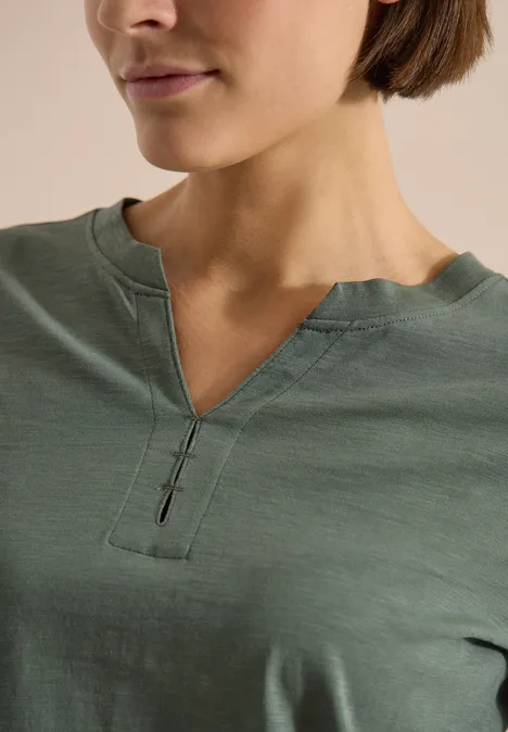 3/4-Arm Shirt mit Split Neck und Elastiksaum dried olive green Nahaufnahme einer Frau im grünen T-Shirt mit V-förmigem Ausschnitt und Knopfdetail.
