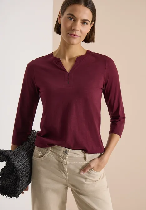 3/4-Arm Shirt mit Split Neck und Elastiksaum red wine Frau in burgunderfarbenem Dreiviertelarmshirt mit V-Ausschnitt, beiger Hose und schwarzem, geflochtenem Korb.