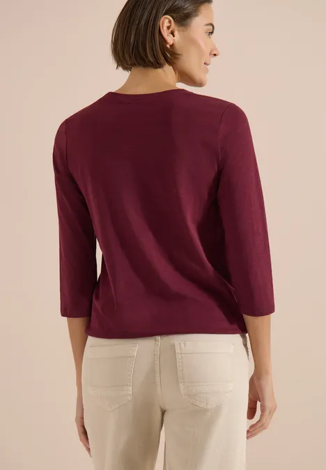 3/4-Arm Shirt mit Split Neck und Elastiksaum red wine Rückansicht einer Frau in einem weinroten Pullover mit 3/4-Ärmeln und weißen Hosen.