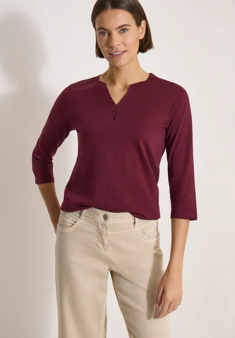 3/4-Arm Shirt mit Split Neck und Elastiksaum red wine Frau trägt burgunderrotes Dreiviertelarm-Oberteil und beige Hose, steht mit Händen in den Taschen vor hellem Hintergrund.