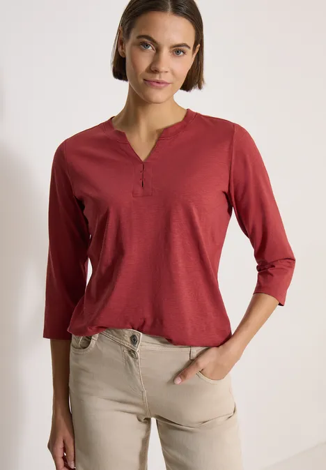 3/4-Arm Shirt mit Split Neck und Elastiksaum russet red Frau trägt kastiges, dunkelrotes 3/4-Arm-Henley-Shirt mit Knopfleiste und eine beigefarbene Hose.