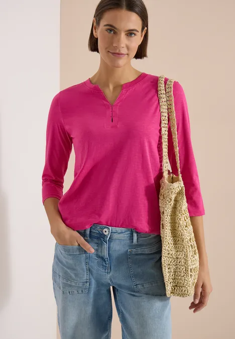 3/4-Arm Shirt mit Split Neck und Elastiksaum pink flash Frau trägt pinkes 3/4-Arm-Shirt, blaue Jeans und hält eine gehäkelte Strohtasche.