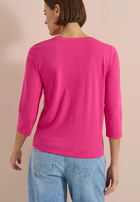 3/4-Arm Shirt mit Split Neck und Elastiksaum pink flash Frau von hinten in pinkem 3/4-Arm-Shirt und blauen Jeans vor beigem Hintergrund.