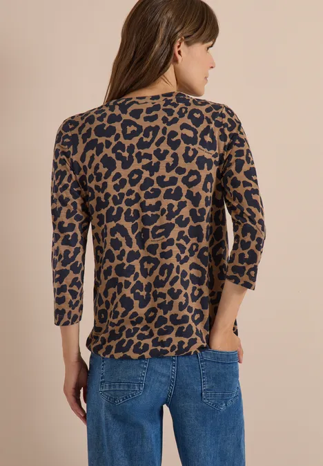 Frau von hinten in blauer Jeans und dreiviertelärmligem Oberteil mit braun-schwarzem Leopardenmuster.
