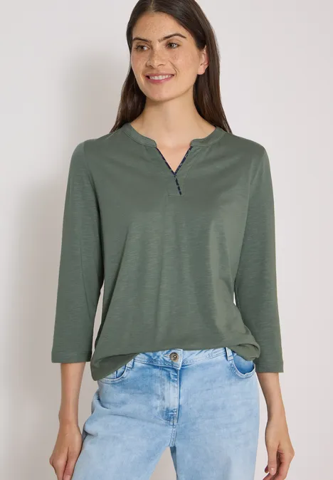 3/4-Arm Shirt mit Split Neck dried olive green Frau lächelnd in grünem Langarmshirt und blauer Jeans vor weißem Hintergrund