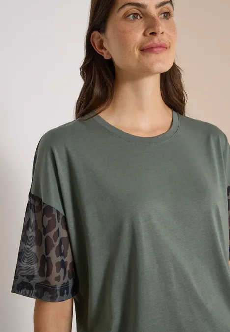 Close-up van een vrouw in een kaki T-shirt met korte mouwen in luipaardprint.