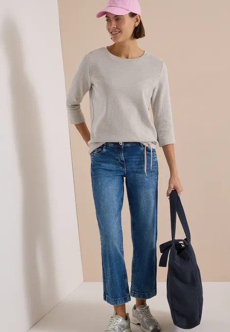 3/4-Arm Shirt mit Rundhals und Struktur natural taupe Frau mit rosa Cap, grauem 3/4-Shirt, blauen Cropped-Jeans, weißen Sneakern und navy-Tasche.