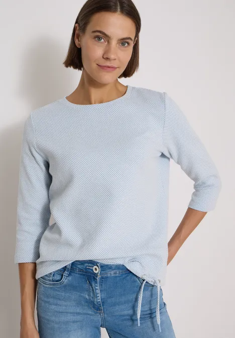 3/4-Arm Shirt mit Rundhals und Struktur easy blue Frau mit schulterlangem Haar in hellblauem Shirt und Jeans vor neutralem Hintergrund.