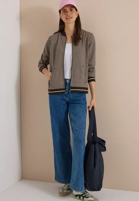 Blouson léger au motif « pepita » raw chocolate brown Eine Frau mit rosa Cap, grauer Bomberjacke, weißem Shirt, weiten Jeans hält eine blaue Tasche.