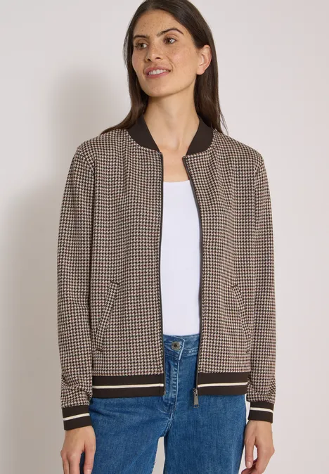 Blouson léger au motif « pepita » raw chocolate brown Frau trägt karierte braune Bomberjacke mit schwarzen Bündchen, weißes Shirt und blaue Jeans.