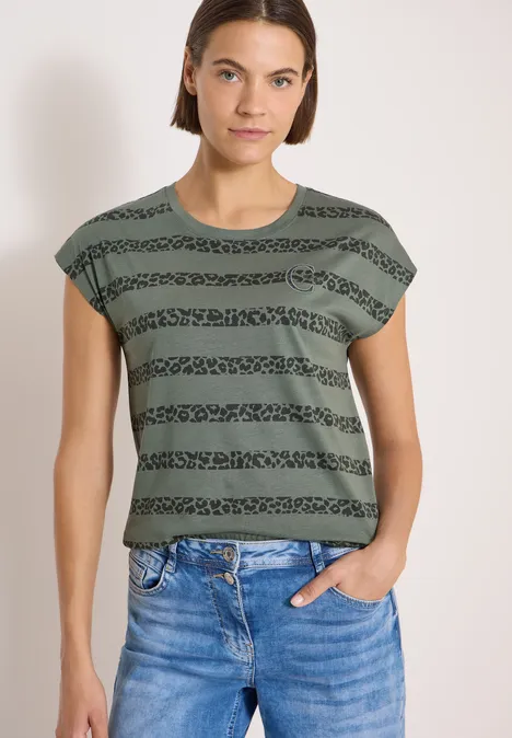 T-Shirt mit Rundhals und Leo-Streifen dried olive green Frau in grünem, gestreiftem kurzärmeligem Oberteil und blauen Jeans, eine Hand in der Hosentasche.