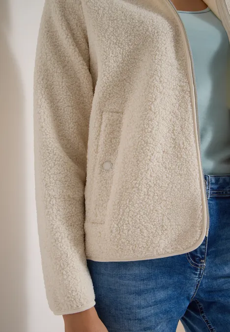 Beige Teddy-Fleecejacke mit Tasche, hellblauem Top und Jeans.