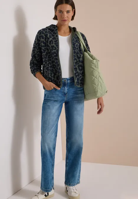 Femme en t-shirt blanc, jean bleu, veste polaire à motif, sac matelassé et baskets blanches.