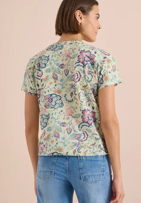 Shirt met split in de hals en print raw matcha lime Vrouw van achteren in een gebloemde top met korte mouwen en een spijkerbroek, neutrale achtergrond.