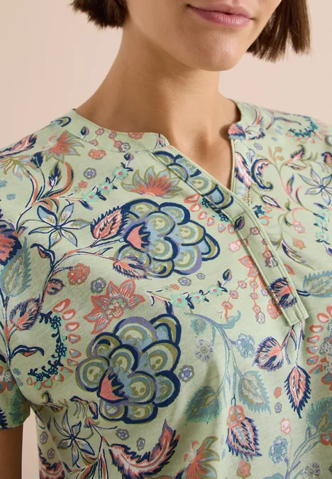Shirt met split in de hals en print raw matcha lime Close-up van een vrouw in een groen shirt met kleurrijke bloemenprint