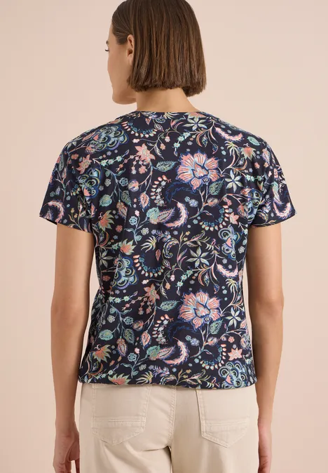 Shirt met split in de hals en print urban dark blue Vrouw van achteren in donkerblauw t-shirt met kleurrijk bloemenpatroon en lichte broek.