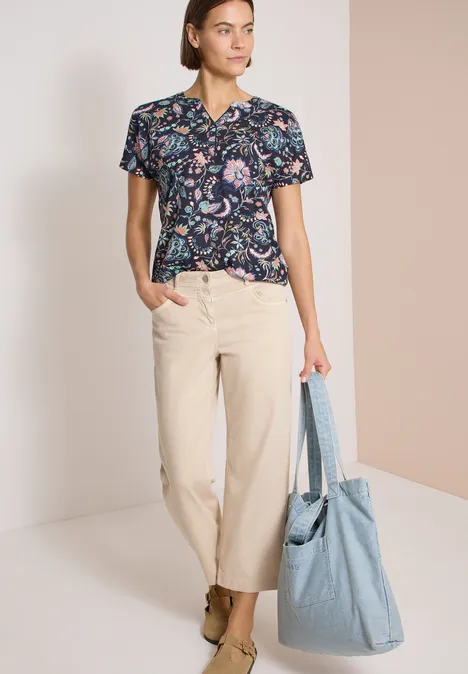 Shirt met split in de hals en print urban dark blue Vrouw met gebloemd shirt, beige broek en grote lichtblauwe tas.