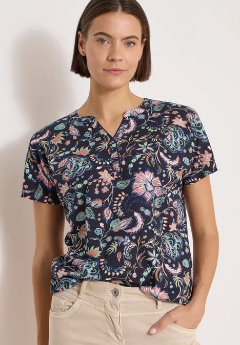 Shirt met split in de hals en print urban dark blue Vrouw in donkerblauw T-shirt met kleurrijk bloemen-paisleymotief en lichte broek, hand in de zak.