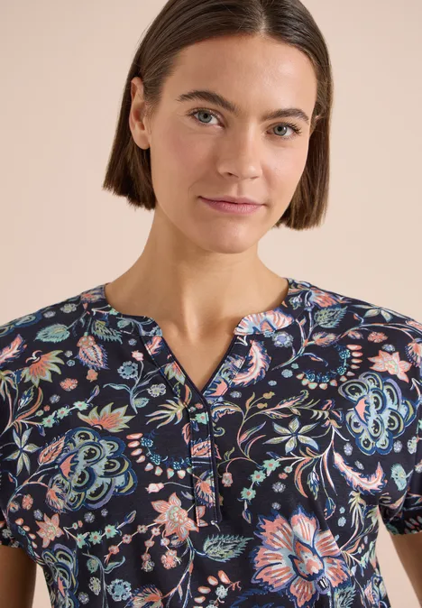 Shirt met split in de hals en print urban dark blue Vrouw met donkerblauw shirt met korte mouwen, kleurig bloemenpatroon en V-hals.