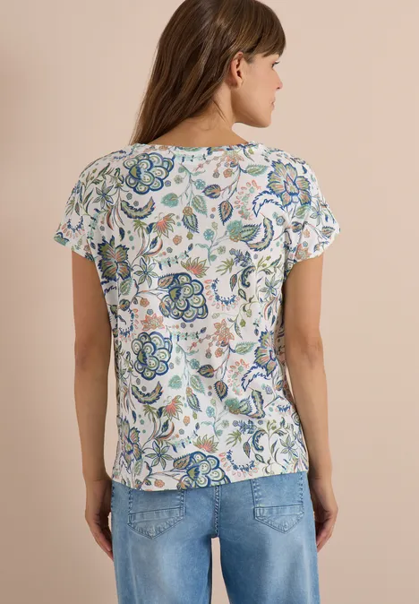 Frau von hinten in weißer kurzärmeliger Bluse mit buntem Blumenmuster und blauen Jeans.