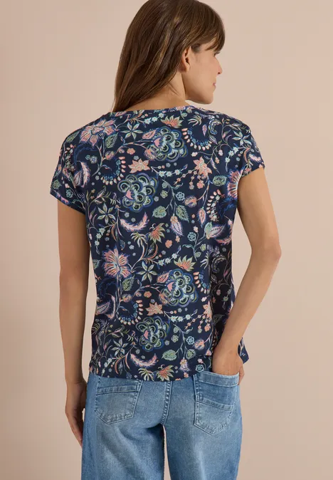 Frau von hinten in dunkelblauem T-Shirt mit buntem Blumenmuster und Jeans.