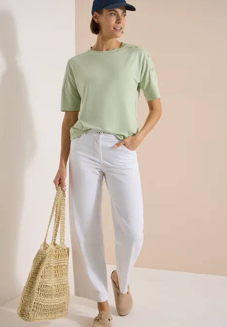 Dropped Shoulder Shirt mit Knöpfen raw matcha lime Frau in mintgrünem T-Shirt, weißen Jeans, Strohtasche und beigen Slippern vor neutralem Hintergrund.