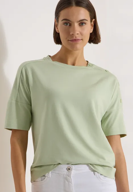 Dropped Shoulder Shirt mit Knöpfen raw matcha lime Frau trägt hellgrünes T-Shirt und weiße Jeans vor weißem Hintergrund.