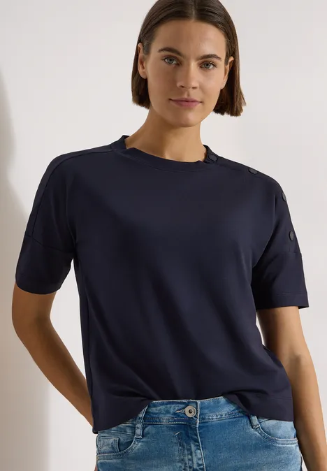 Chemise à épaules tombantes avec boutons urban dark blue Eine Person in dunkelblauem T-Shirt und Jeans vor hellem Hintergrund.