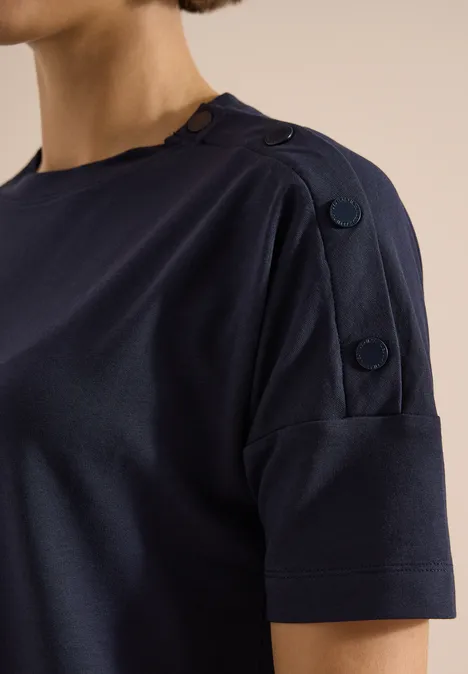 Chemise à épaules tombantes avec boutons urban dark blue Frau in dunkelblauem T-Shirt mit kurzem Ärmel und dekorativen Knöpfen an der Schulter.