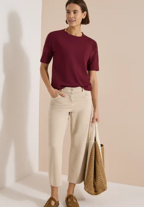 Dropped Shoulder Shirt mit Knöpfen red wine Frau in weinrotem T-Shirt, hellen, weiten Jeans und Korbtasche vor neutralem Hintergrund.