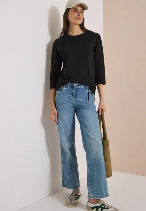 3/4-Arm Shirt mit Rundhals in Unifarbe Black Frau trägt schwarzes Langarmshirt, helle Jeans, weiße Cap, olivgrünen Shopper und Sneaker.
