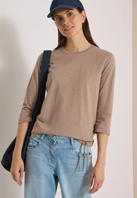 3/4-Arm Shirt mit Rundhals in Unifarbe natural taupe Frau in beige 3/4-Arm-Shirt, hellblauen Jeans und dunkler Umhängetasche.