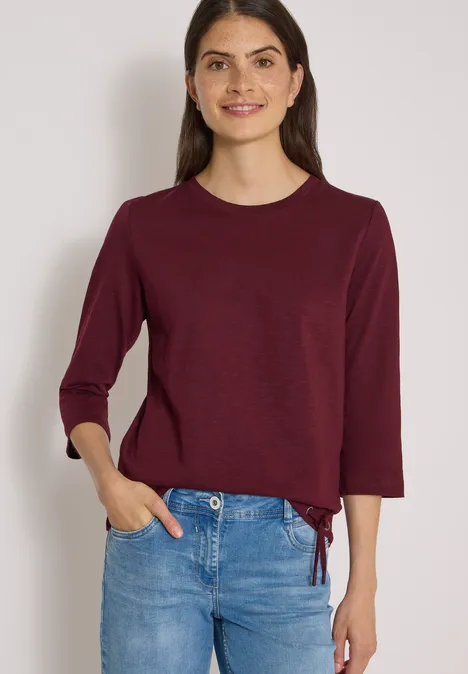 3/4-Arm Shirt mit Rundhals in Unifarbe red wine Dame in blauem Jeans und burgunderrotem Langarm-Shirt, das an der Taille gebunden ist.