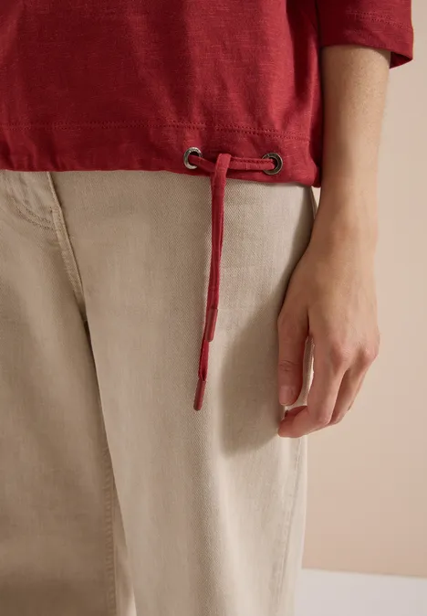 3/4-Arm Shirt mit Rundhals in Unifarbe russet red Nahaufnahme einer Person mit rotem Shirt, beigen Hosen und einer herabhängenden Kordel.