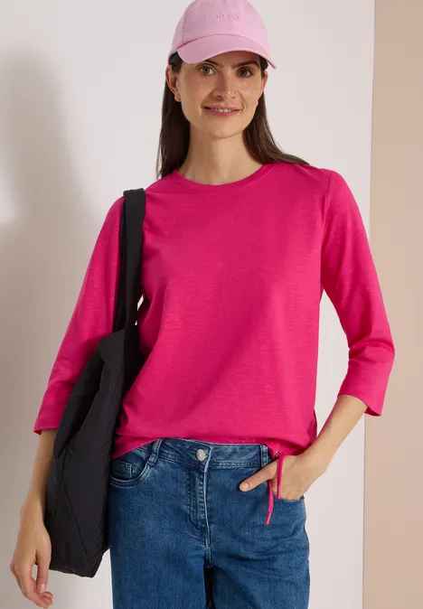 3/4-Arm Shirt mit Rundhals in Unifarbe pink flash Junge Frau in pinkem Pullover und Cap, blauer Jeans, mit schwarzer Tasche auf der Schulter.
