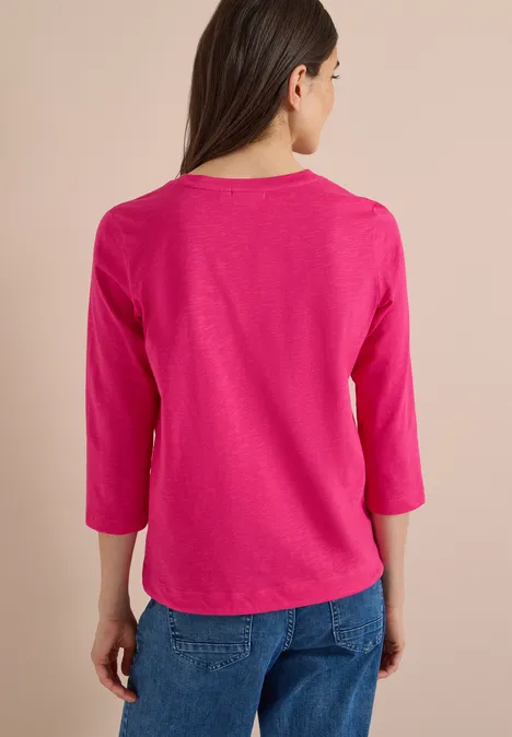 3/4-Arm Shirt mit Rundhals in Unifarbe pink flash Frau von hinten in pinkem 3/4-Arm-Shirt und blauen Jeans vor hellem Hintergrund.