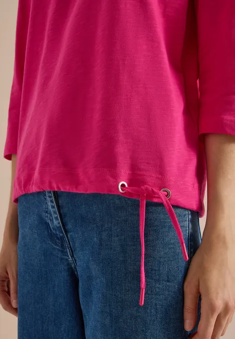 3/4-Arm Shirt mit Rundhals in Unifarbe pink flash Eine Person trägt ein pinkes Shirt mit seitlichen Kordelzügen und blaue Jeans.