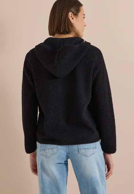 Rückansicht einer Person in schwarzem Kapuzenpulli und blauen Jeans.