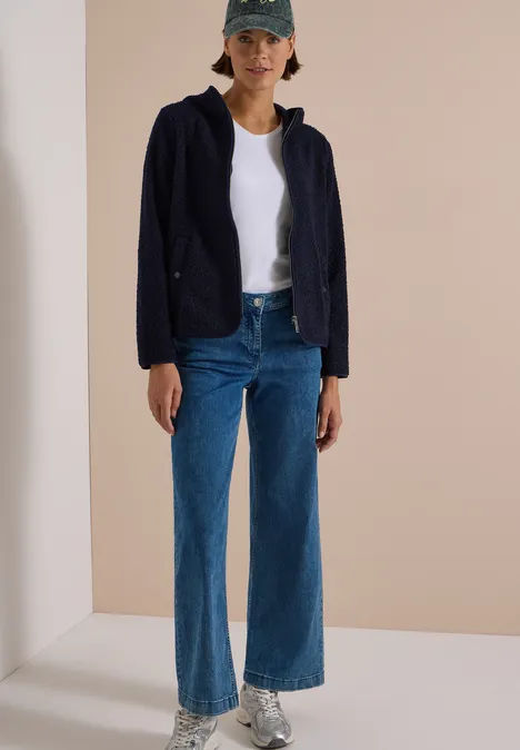 Frau mit Baseballcap, weißem T-Shirt, dunkelblauer Jacke, weitem Jeanshose und Sneakern