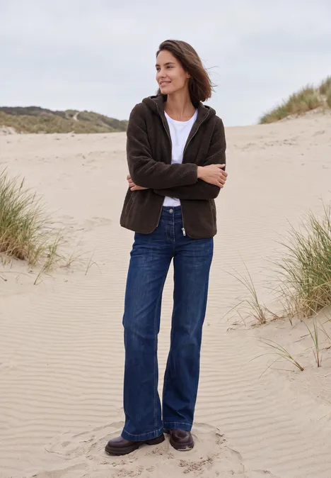 Teddy-Jacke mit Kapuze in Unifarbe truffle brown Frau in Jeans und Jacke steht entspannt mit verschränkten Armen auf Dünen am Strand.