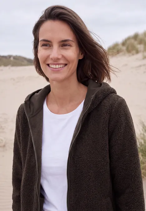 Teddy-Jacke mit Kapuze in Unifarbe truffle brown Eine lächelnde Frau in einem Fleece-Pullover steht am Strand mit Dünen im Hintergrund.