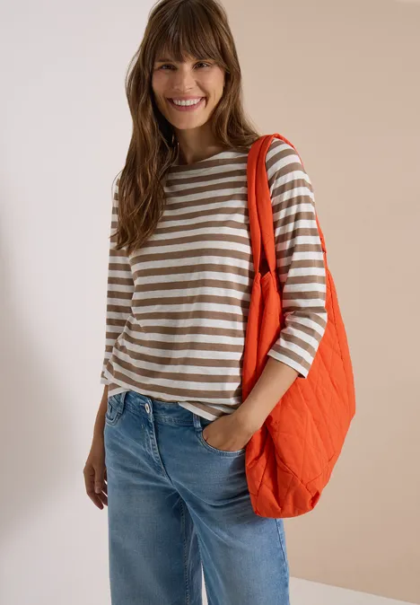 T-shirt basique à col bateau et rayures natural taupe Frau mit gestreiftem Shirt, Jeans und großer oranger Umhängetasche lächelt in die Kamera.
