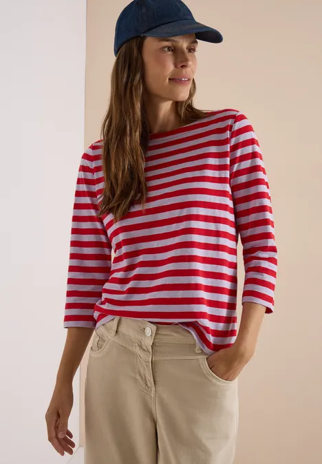 Frau in rot-weiß gestreiftem Shirt, beiger Hose und Baseballcap.