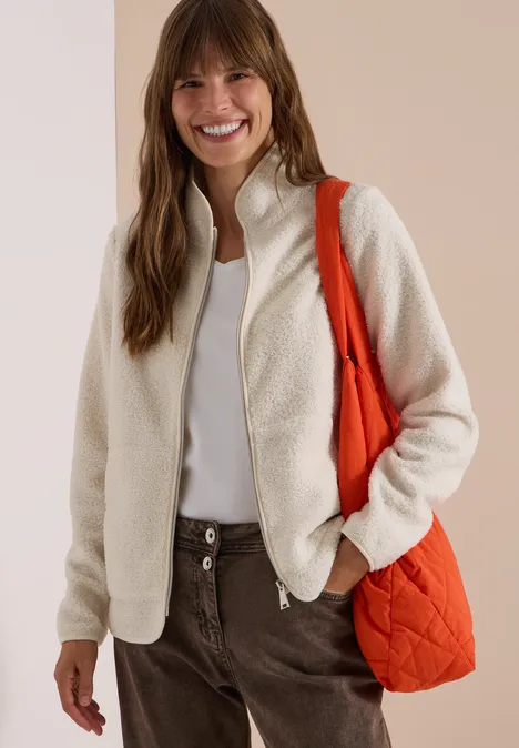 Frau lächelt in cremefarbener Teddy-Fleecejacke mit orangefarbener Tasche