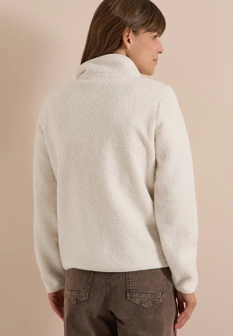 Eine Person trägt eine cremefarbene Teddy-Fleecejacke mit Stehkragen, Rückenansicht.
