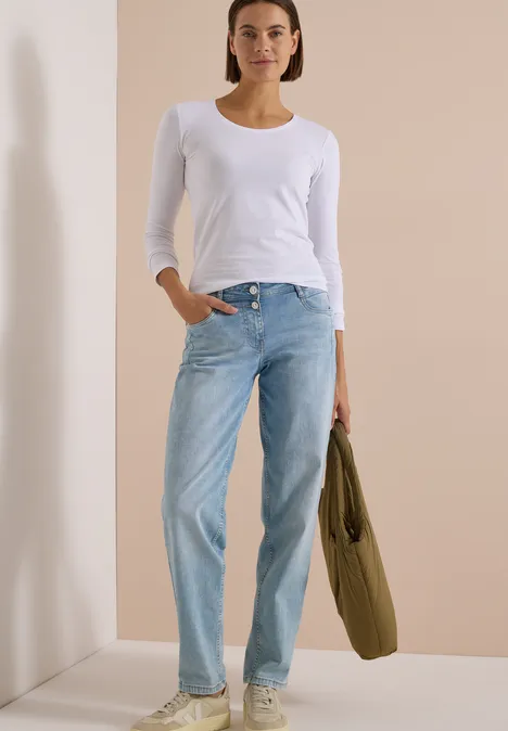Basic Shirt mit Rundhals im 2er-Pack urban dark blue/white Frau in weißen Langarmshirt und blauen Jeans, hält grünen Beutel, stehend vor hellem Hintergrund.